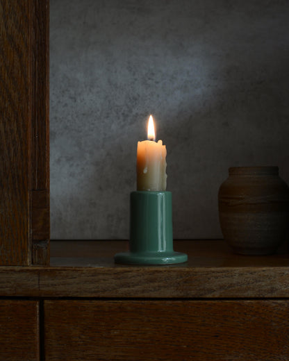 A beeswax candle in a green ceramic holder, on a wooden surface with a dark background