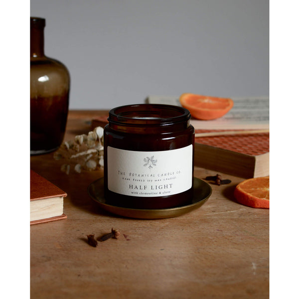 Half Light Scented Soy Candle in amber jar, surrounded by orange slices and cloves..