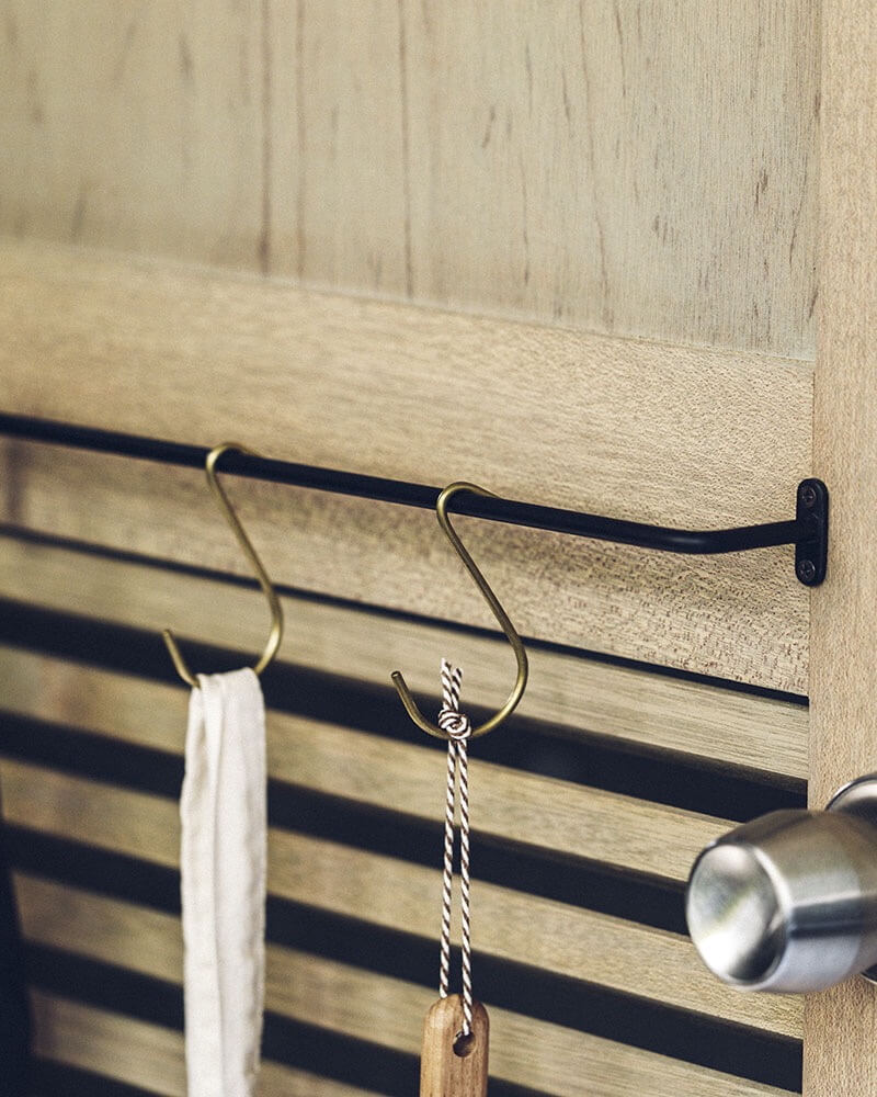 A black iron wall-mounted hanging rail with brass S hooks.