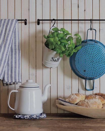 A black iron wall-mounted hanging rail with hanging plant and cooking utensils.
