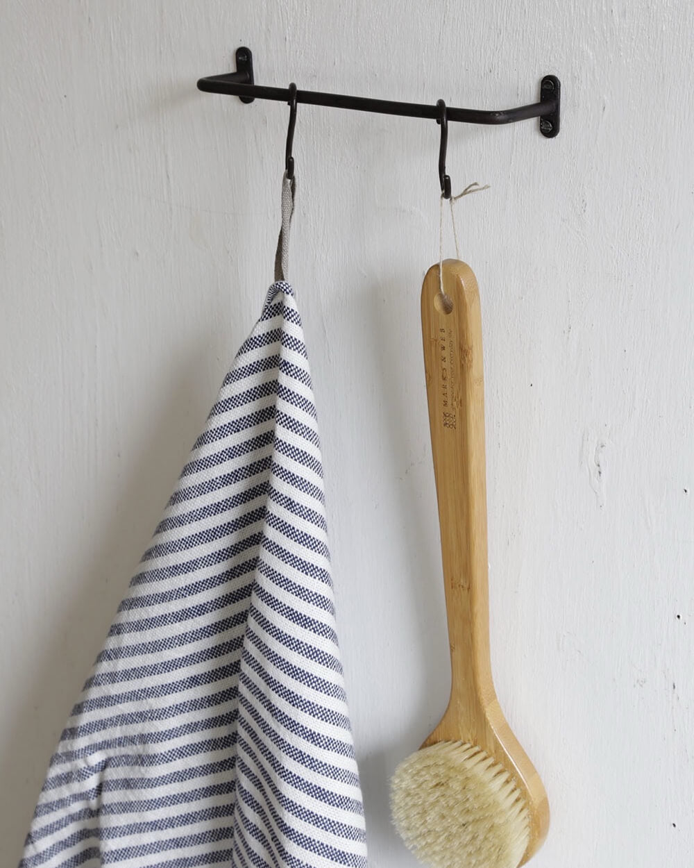 A solid iron, black powder-coated towel rail, shown in a bathroom holding towels and a bath brush.