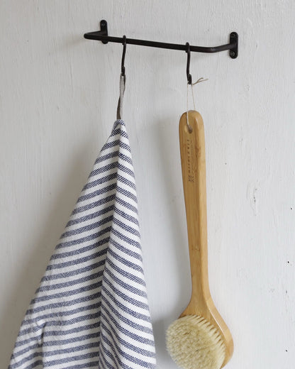 A solid iron, black powder-coated towel rail, shown in a bathroom holding towels and a bath brush.