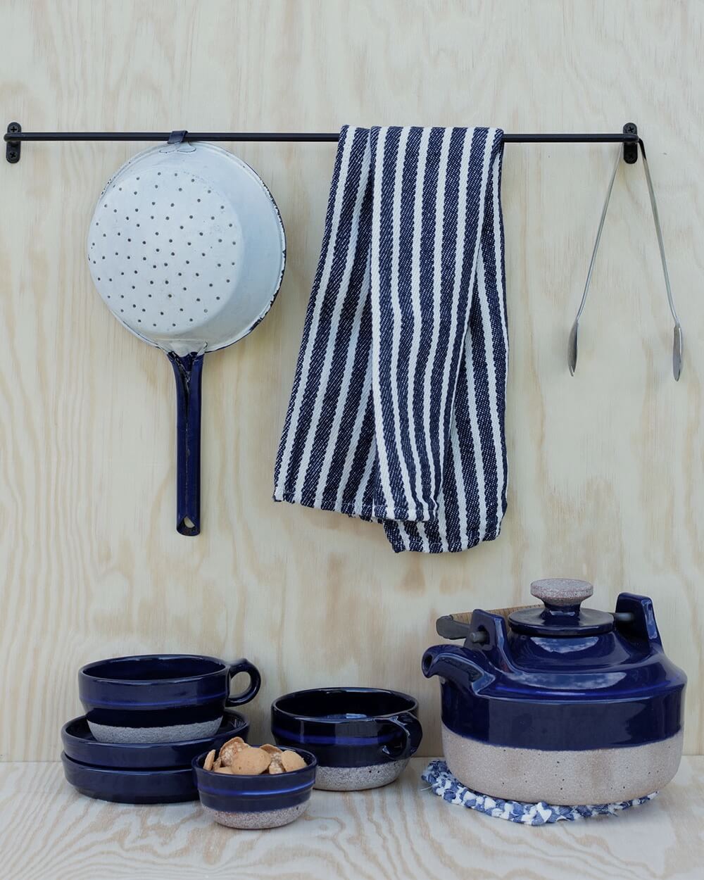 A black iron wall-mounted hanging rail with utensils and tea towels.