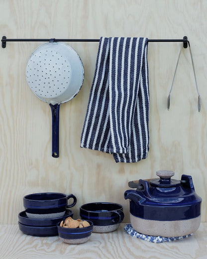 A black iron wall-mounted hanging rail with utensils and tea towels.