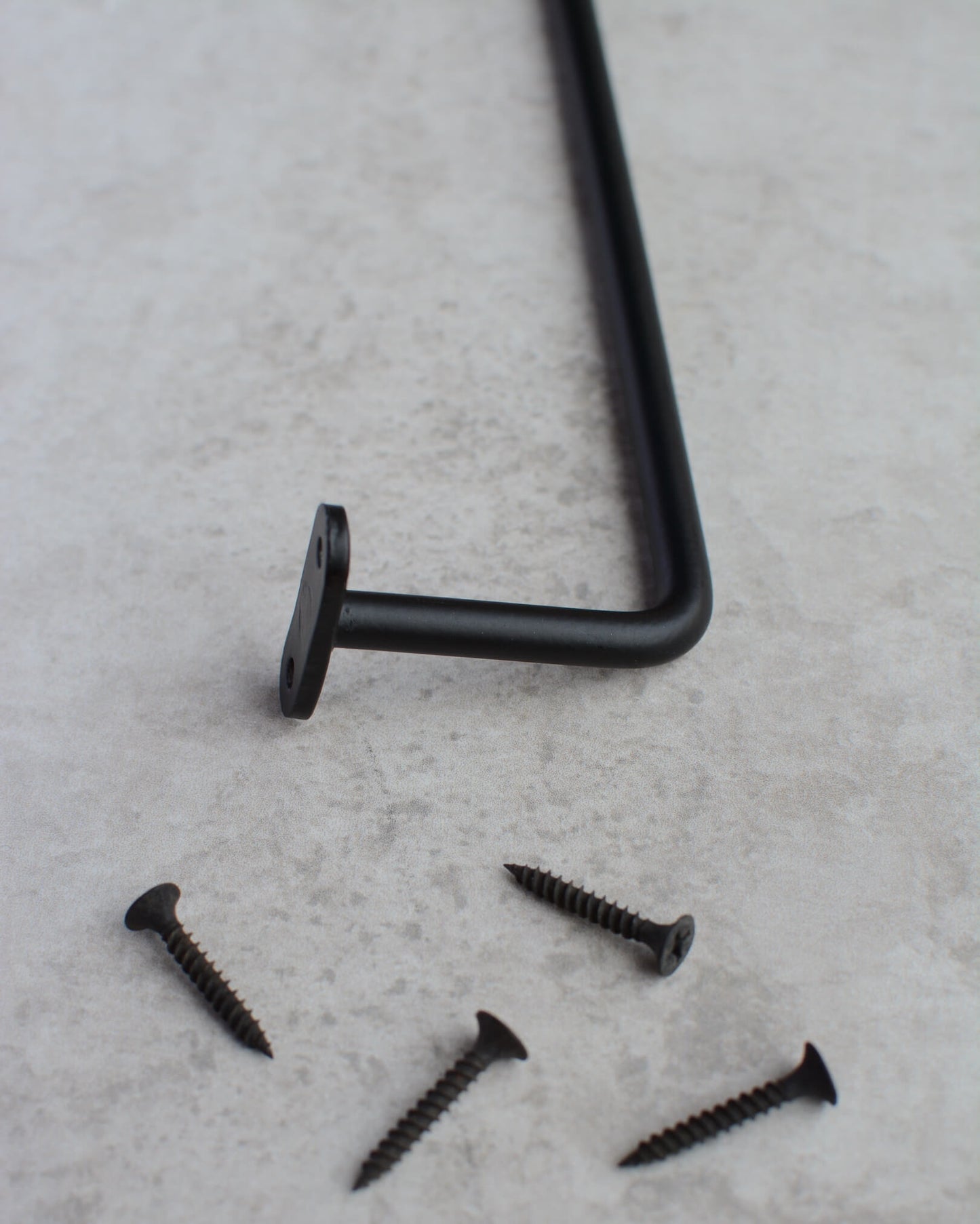 A close-up of a black iron wall-mounted hanging rail and screws.