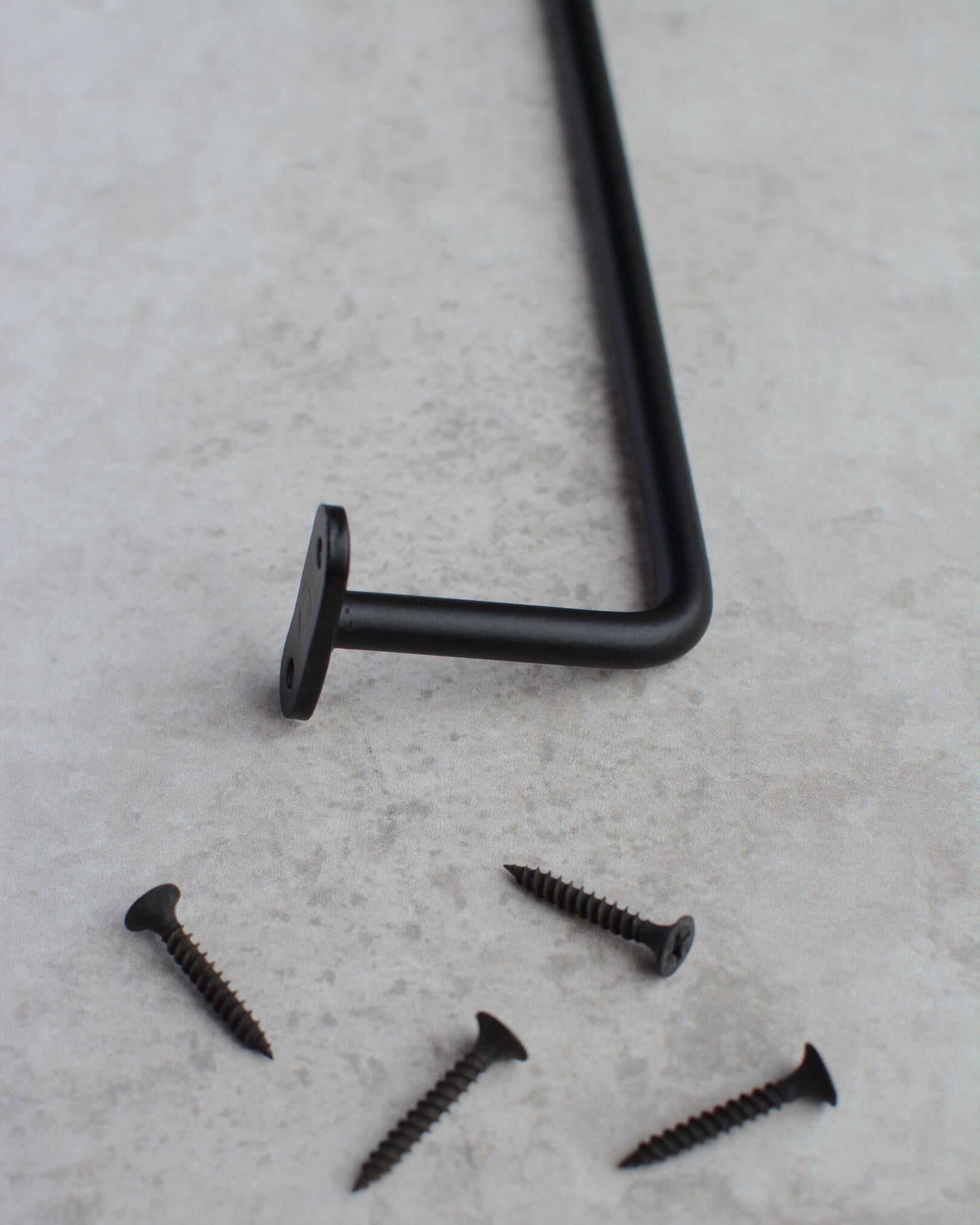 A close-up of a black iron wall-mounted hanging rail and screws.