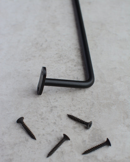 A close-up of a black iron wall-mounted hanging rail and screws.