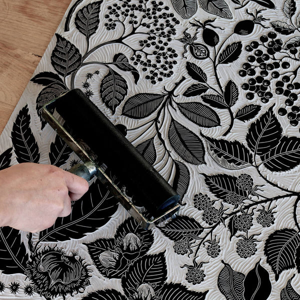 An inked linocut block, depicting seasonal plants and flowers.