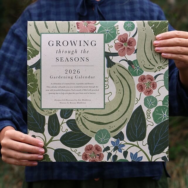 Close up of a person holding a botanical illustration 2026 calendar with the words "Growing through the Seasons".