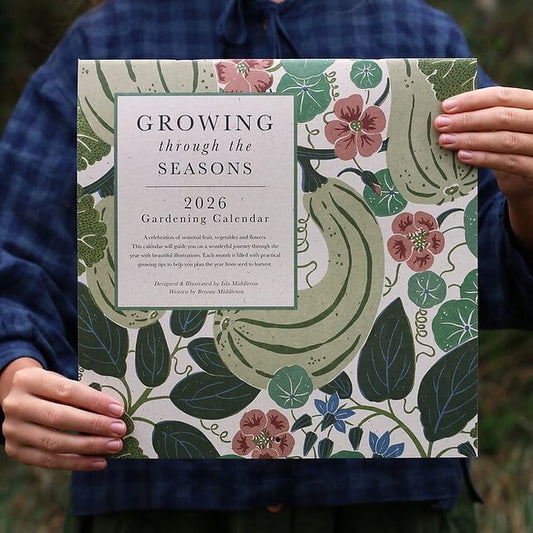 Close up of a person holding a botanical illustration 2026 calendar with the words "Growing through the Seasons".
