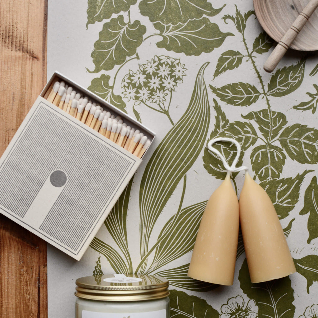 Green botanical 'Spring' linocut print with box of white-tipped matches and pair of short beeswax candles.