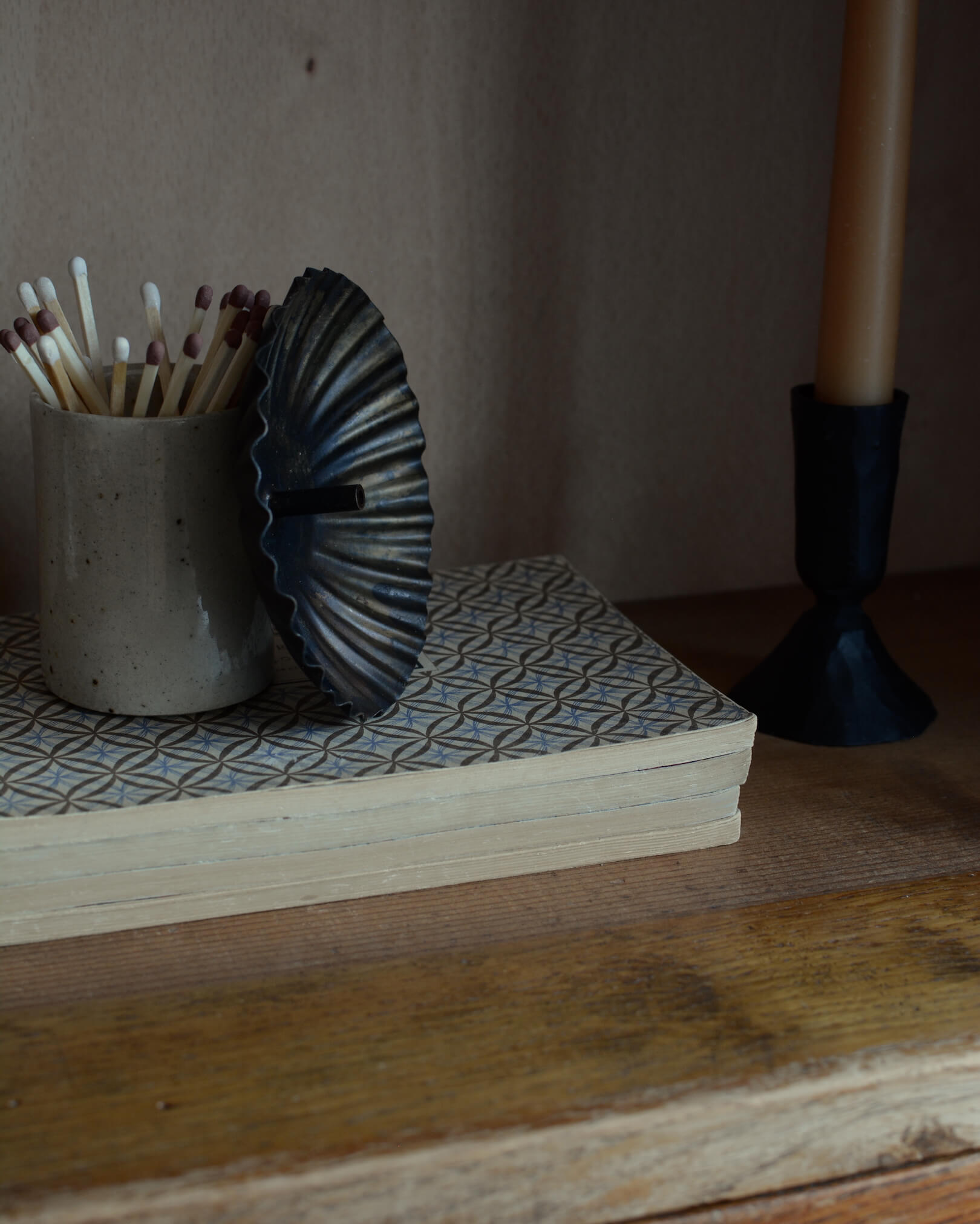 A metal incense holder in a fluted circle design, with a bronzed finish. Next to a ceramic match pot and beeswax candle.