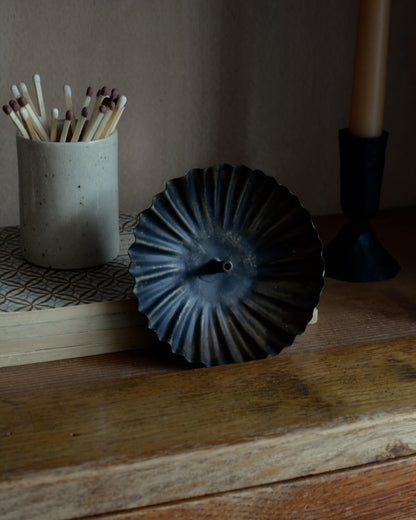 A metal incense holder in a fluted circle design, with a bronzed finish.