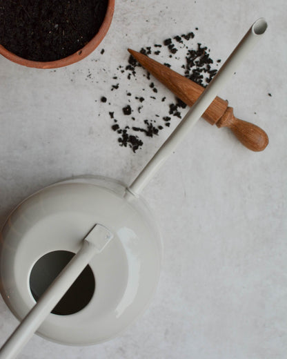 A pale grey watering can from above, next to a terracotta plant pot and seed dibber. 