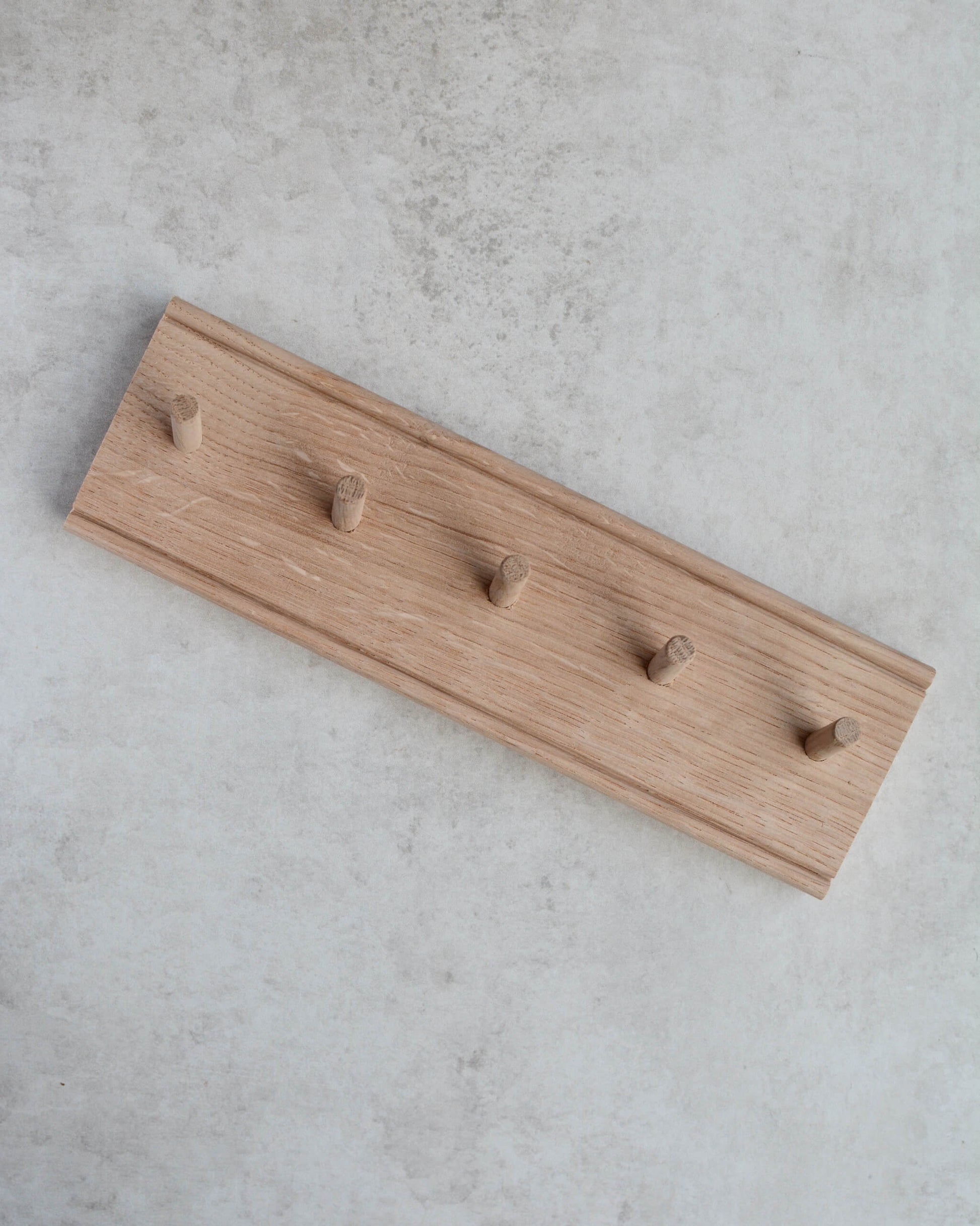 An oak key rack with 5 hooks by Creamore Mill, on a grey surface