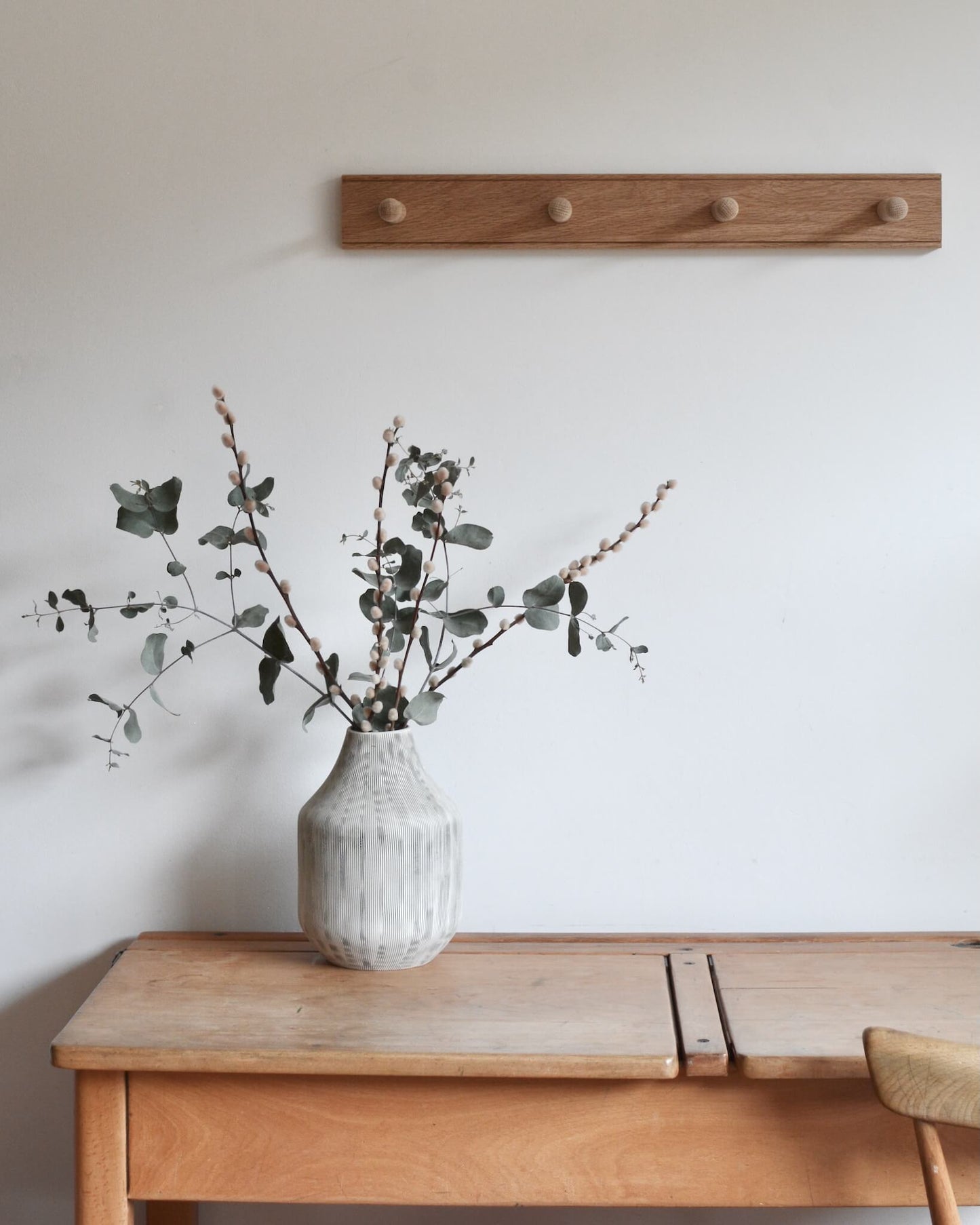 A 4-peg oak shaker peg rail, above a desk with a vase on top.