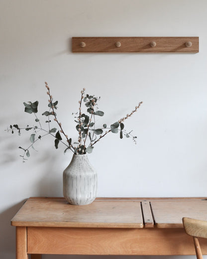 A 4-peg oak shaker peg rail, above a desk with a vase on top.