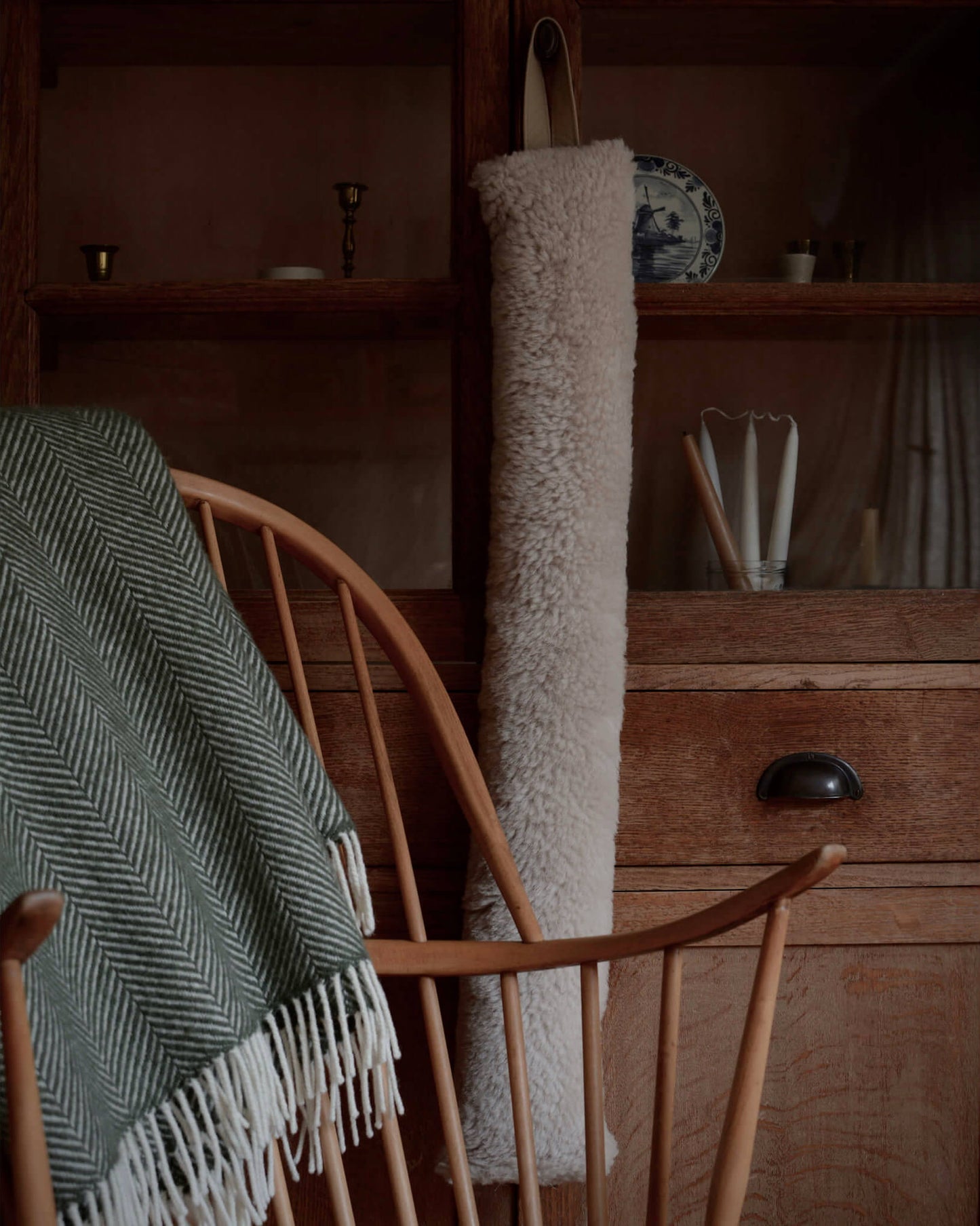 Wooden chair with a green blanket draped over it, and a sheepskin draught excluder displayed behind.