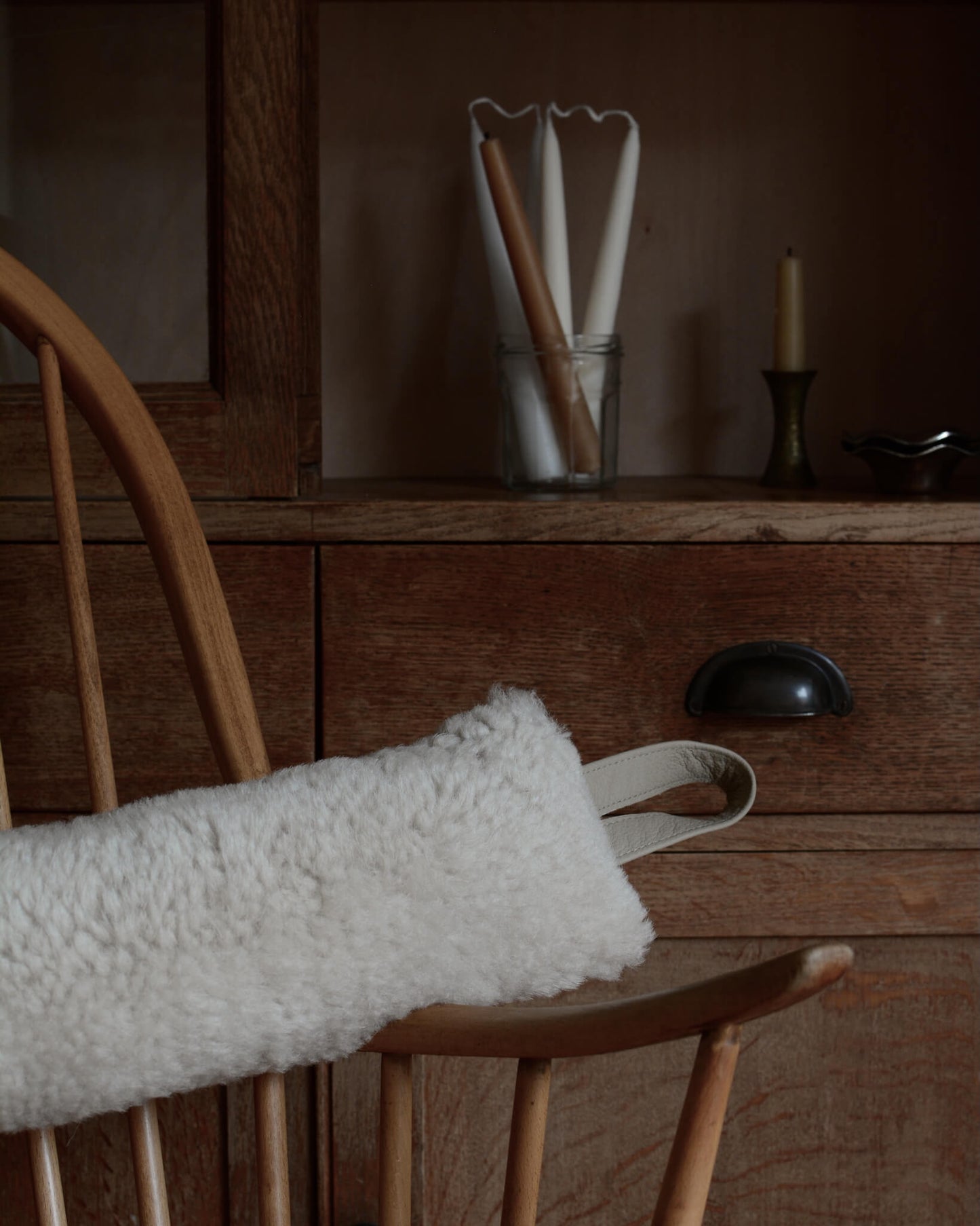 Wooden chair with a cream sheepskin draught excluder draped over it, against a wooden dresser background.