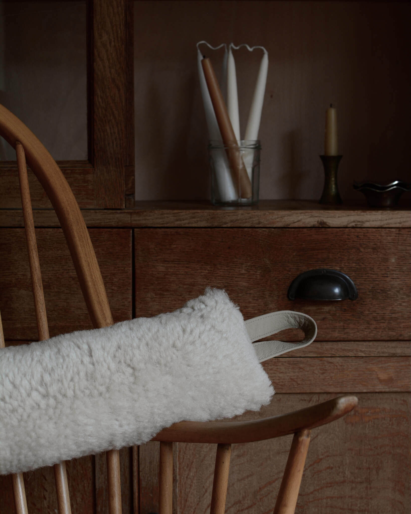 Wooden chair with a cream sheepskin draught excluder draped over it, against a wooden dresser background.