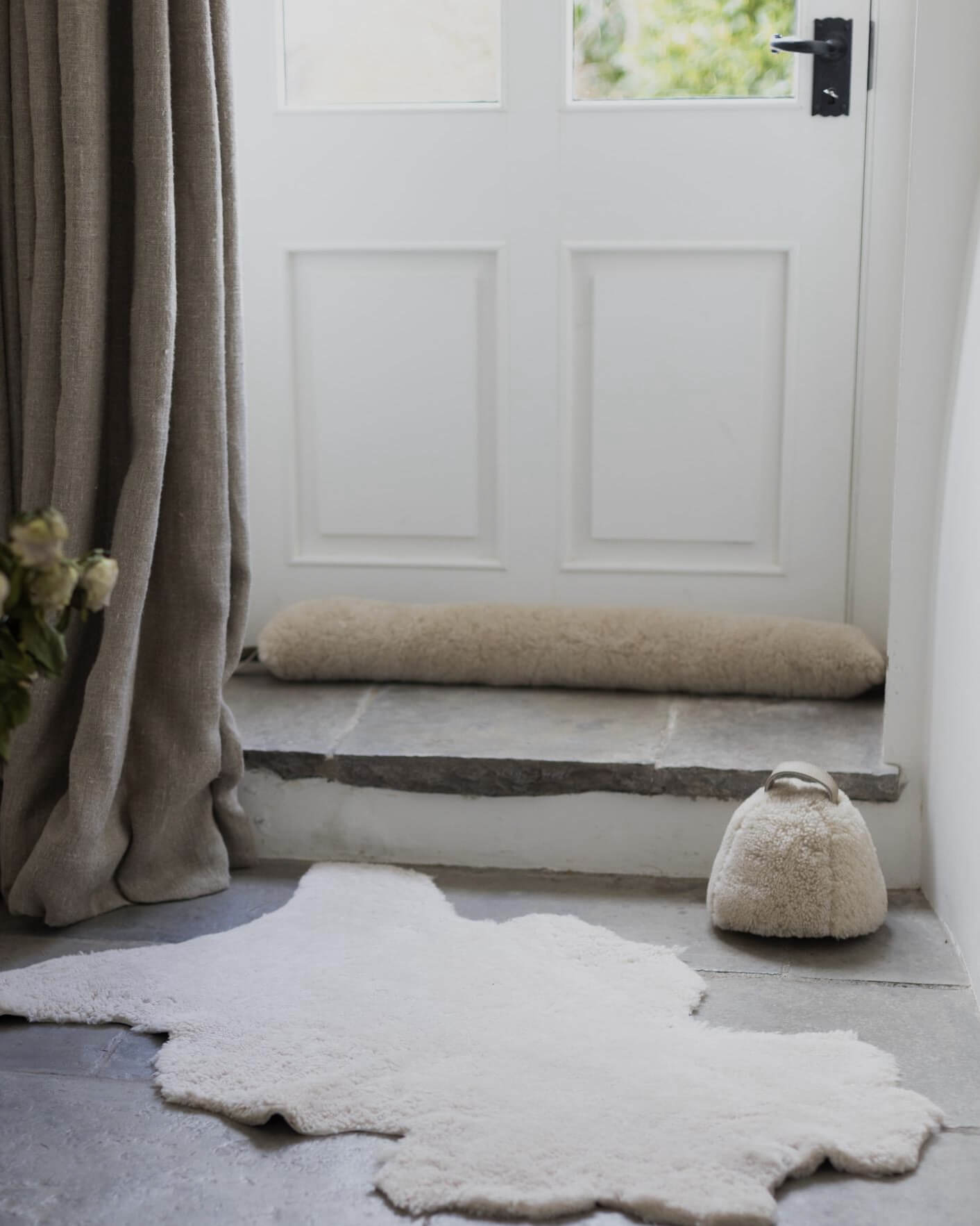 White door with a sheepskin draught excluder, with a rug on the floor and a curtain to the side.