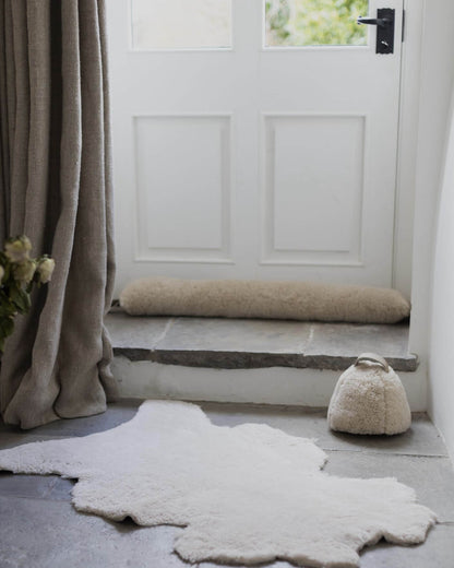 White door with a sheepskin draught excluder, with a rug on the floor and a curtain to the side.