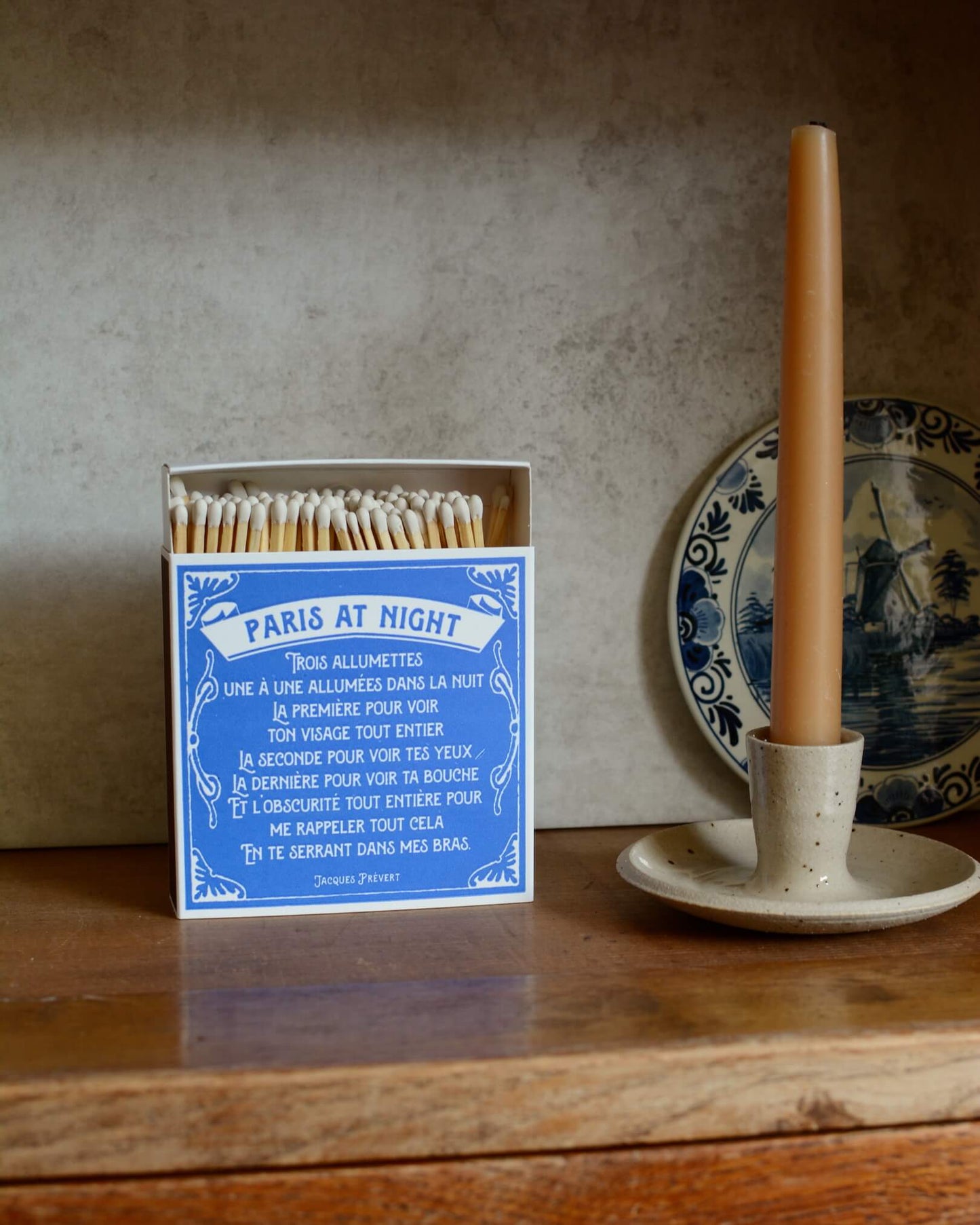 Blue and white matchbox, next to a beeswax candle and ceramic candle holder.