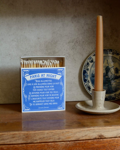 Blue and white matchbox, next to a beeswax candle and ceramic candle holder.