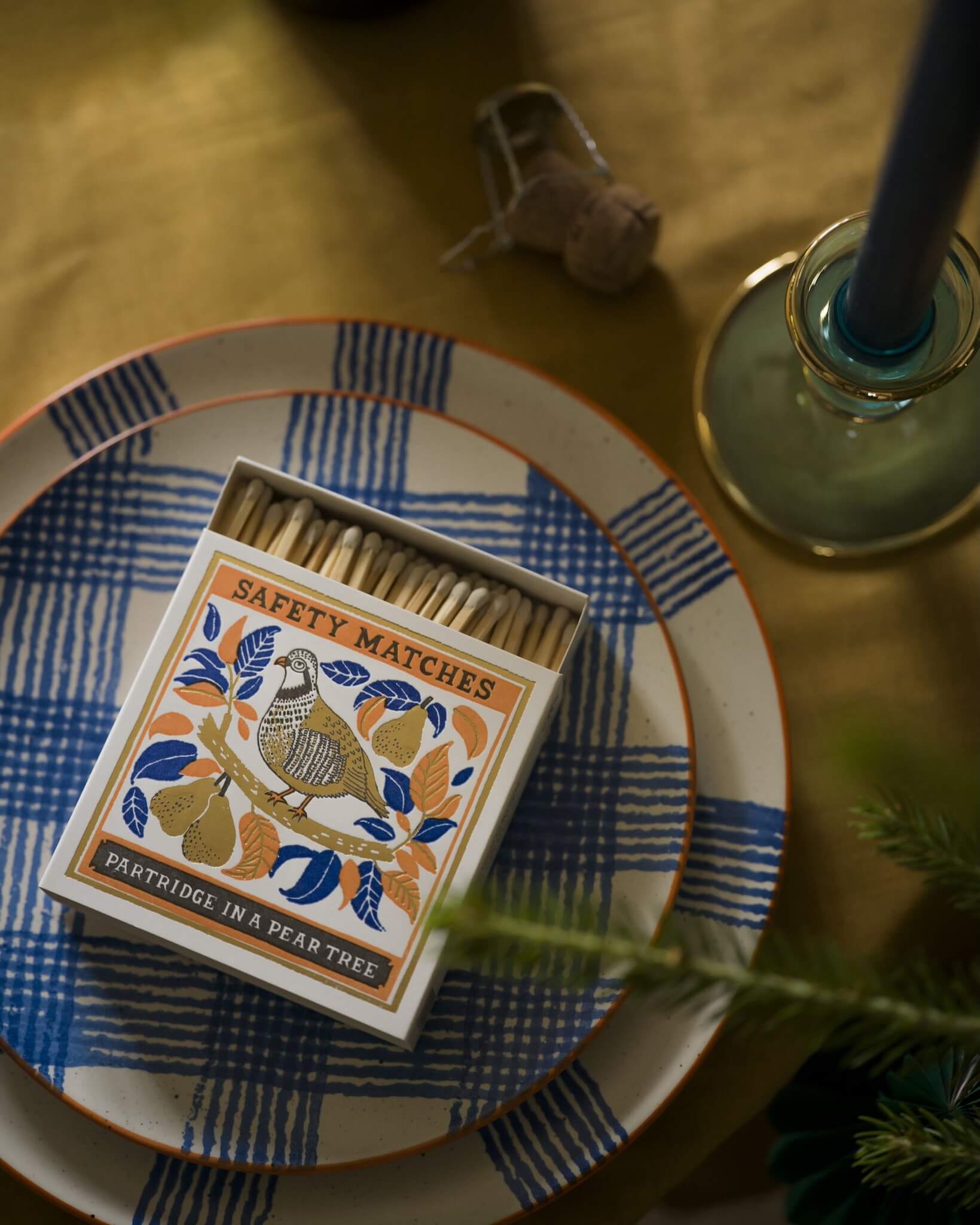 Matches box with decorative design on a table with a candle and checked plates.