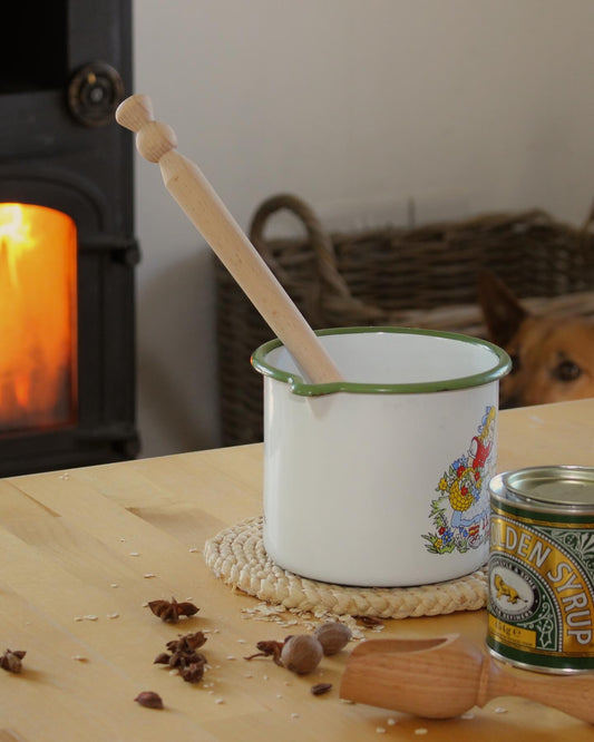 A wooden porridge spurtle, shown with vintage enamelware in a cosy kitchen scene.