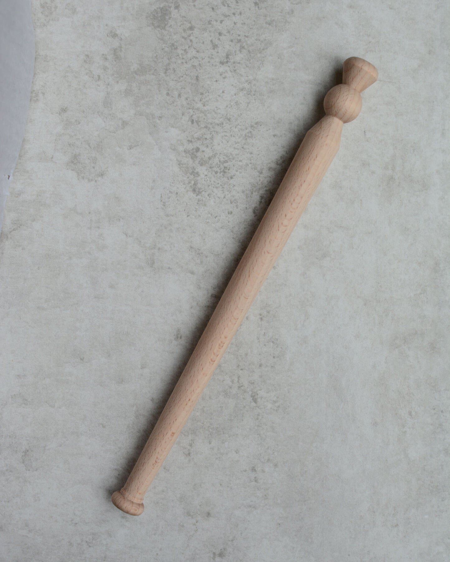 A wooden porridge spurtle, shown on a grey background.