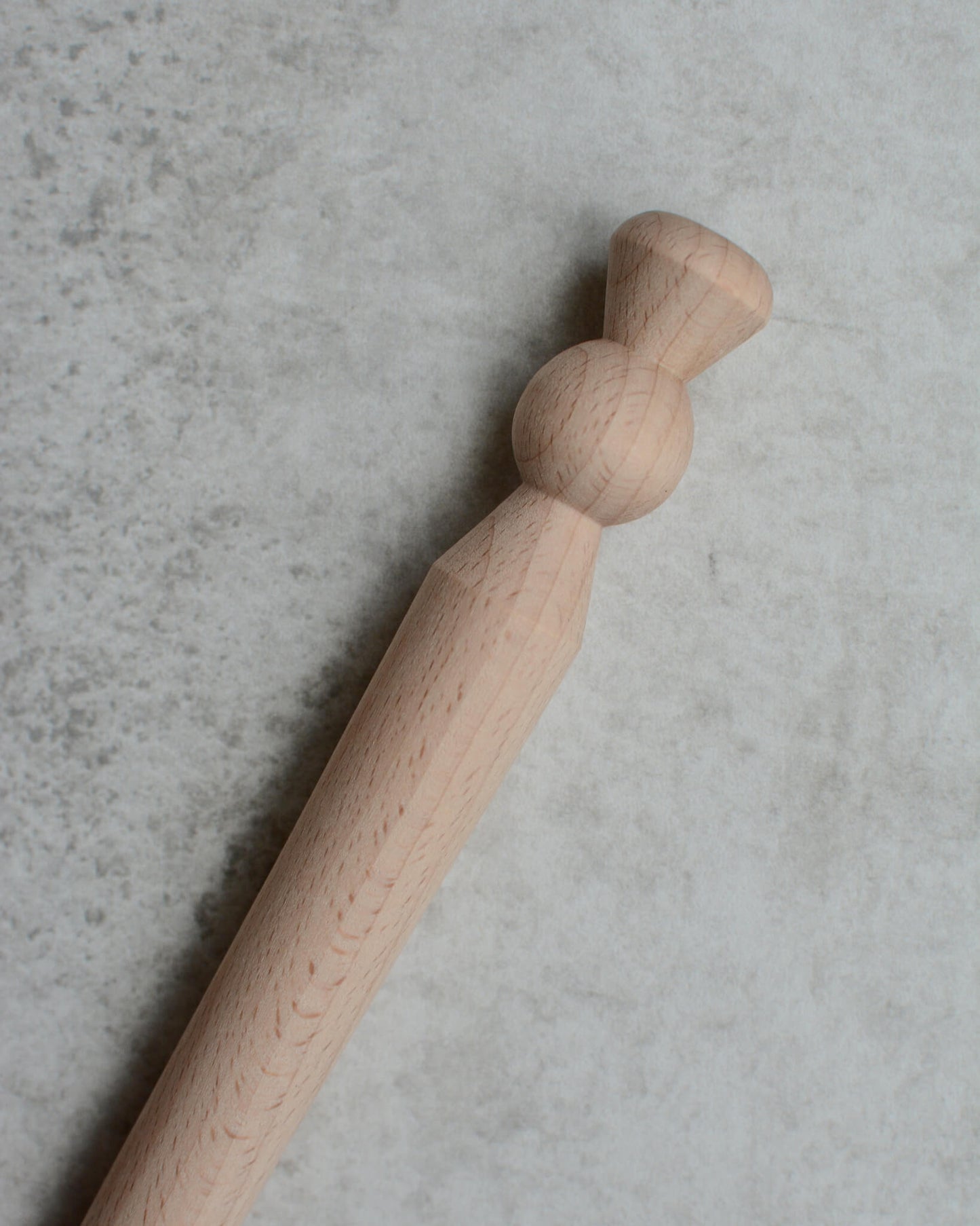 A wooden porridge spurtle, shown on a grey background.