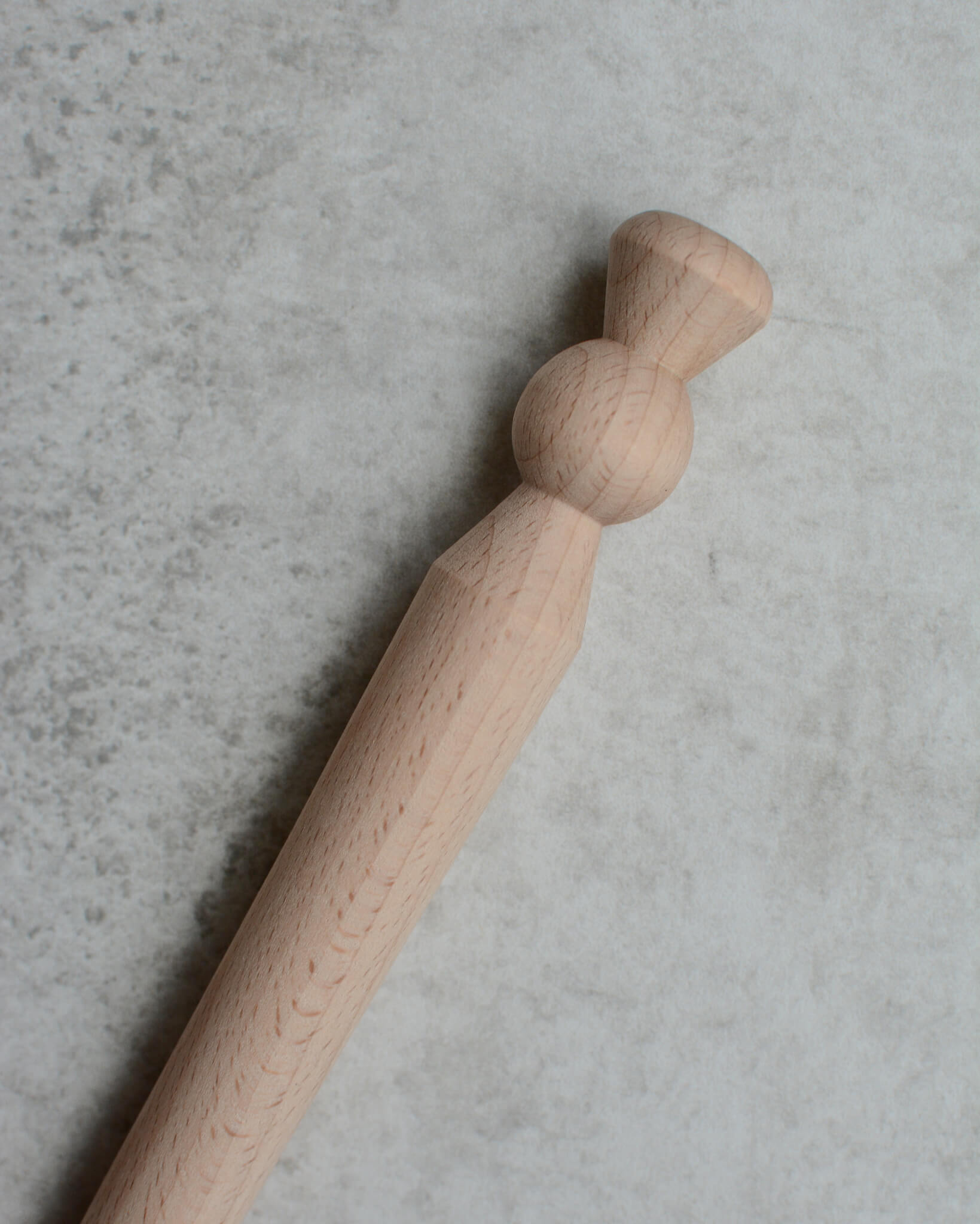 A wooden porridge spurtle, shown on a grey background.