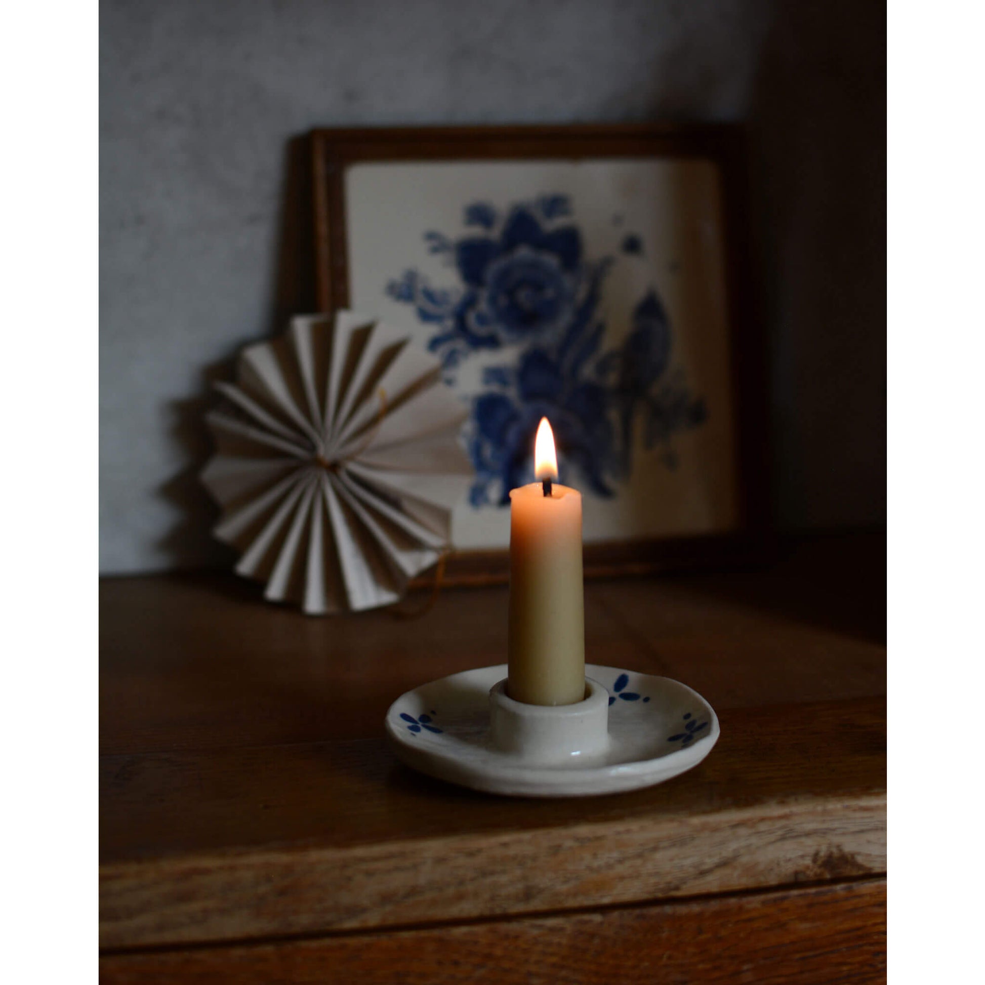 Styled image, featuring a white and blue ceramic candle holder with a lit beeswax candle.