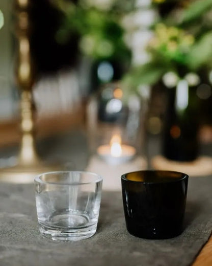 Two glass tealight cups, one clear and one olive green, on a table.
