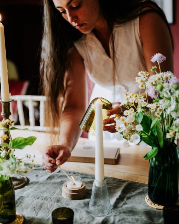 Woman arranging candles and flowers on a table with a warm, indoor setting.