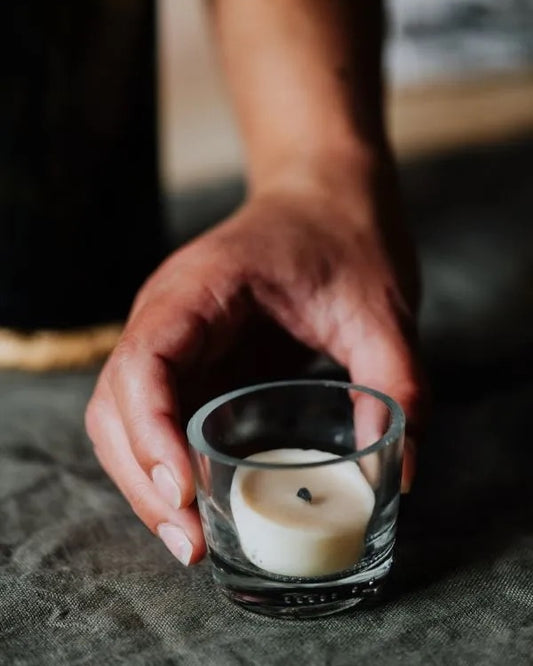 Hand holding a small glass tealight cup, with a candle on a textured surface.