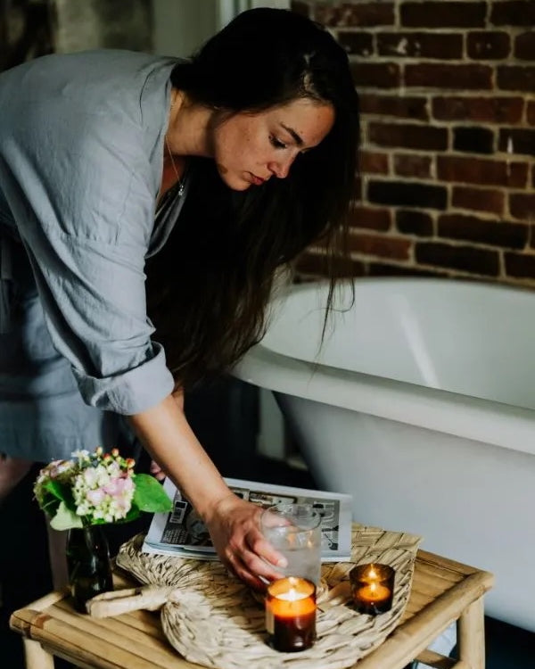 A woman setting a table with candles, in a bathroom.