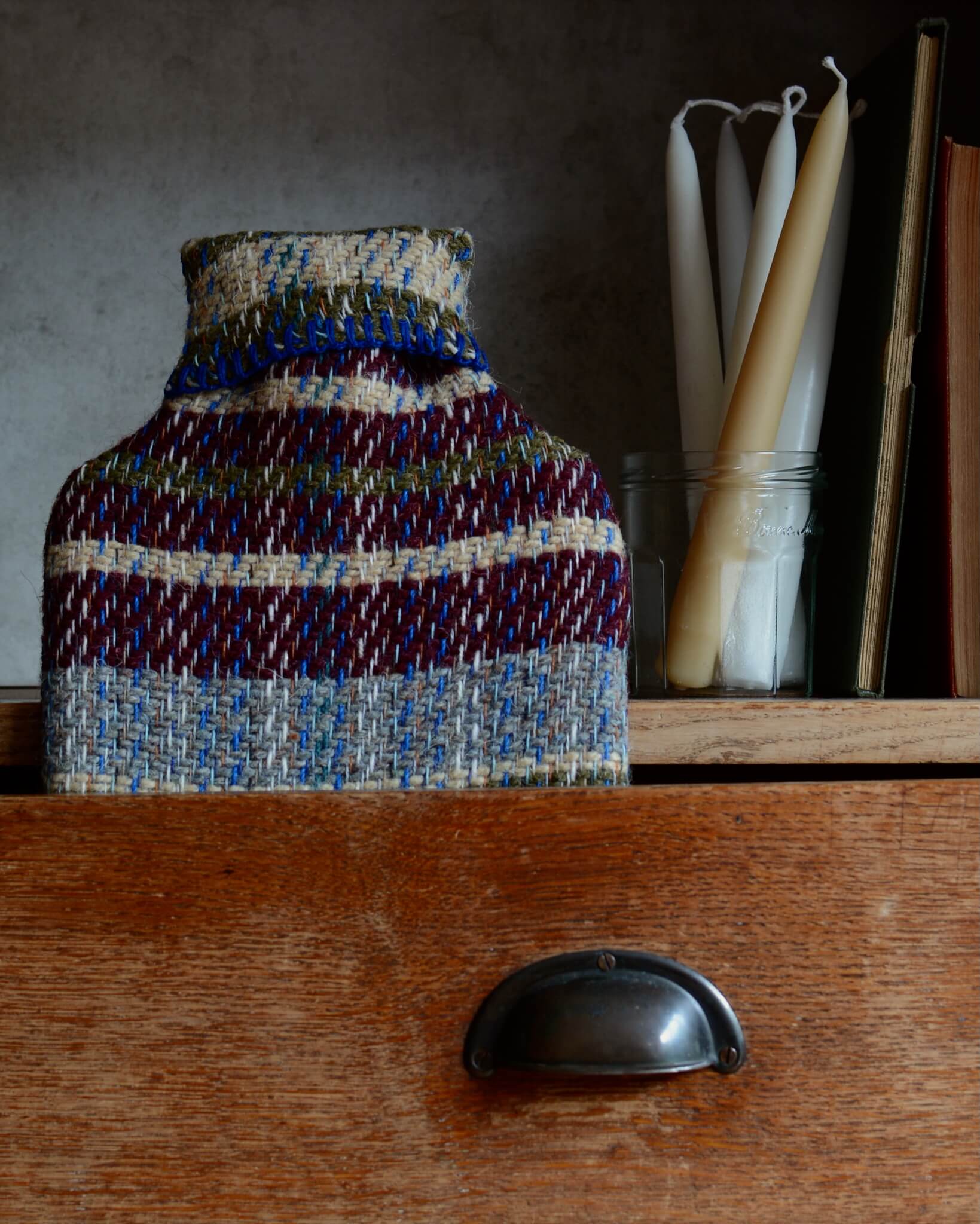 Recycled wool hot water bottle on a wooden surface, with candles in the background.
