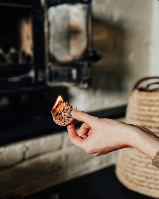 Hand holding a firelighter over a fire with a rustic background.