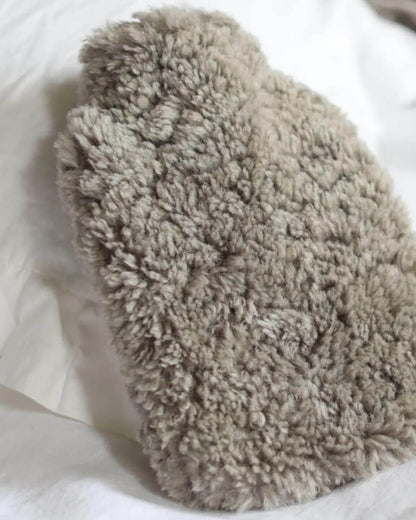 Pale grey sheepskin hot water bottle cover, shown on white bed linen.