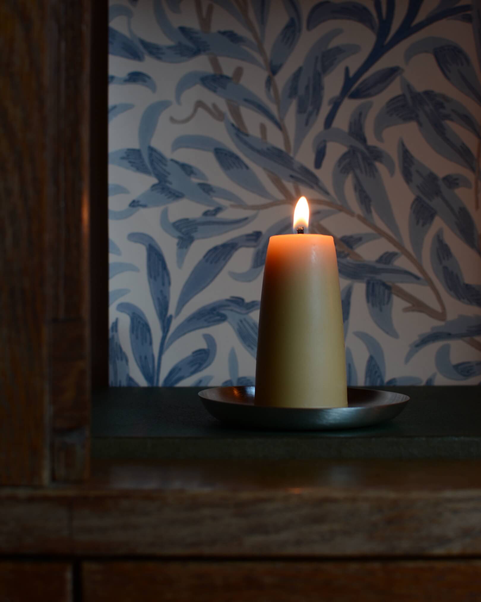 A circular silver-plated candle dish, with a lit beeswax candle.