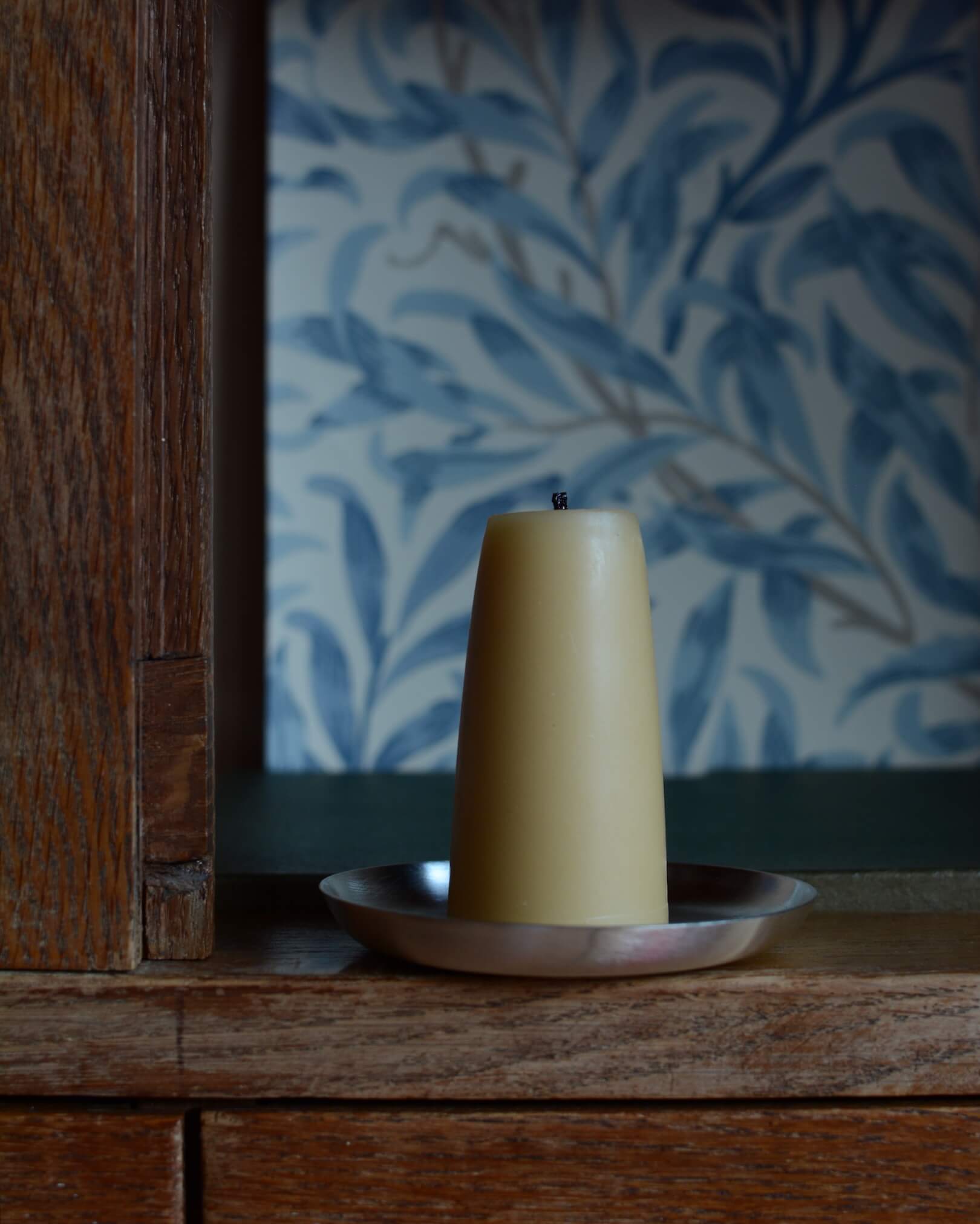 A circular silver-plated candle dish, with a beeswax candle.