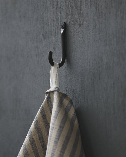 Black iron wall hook with a striped towel on a grey wall