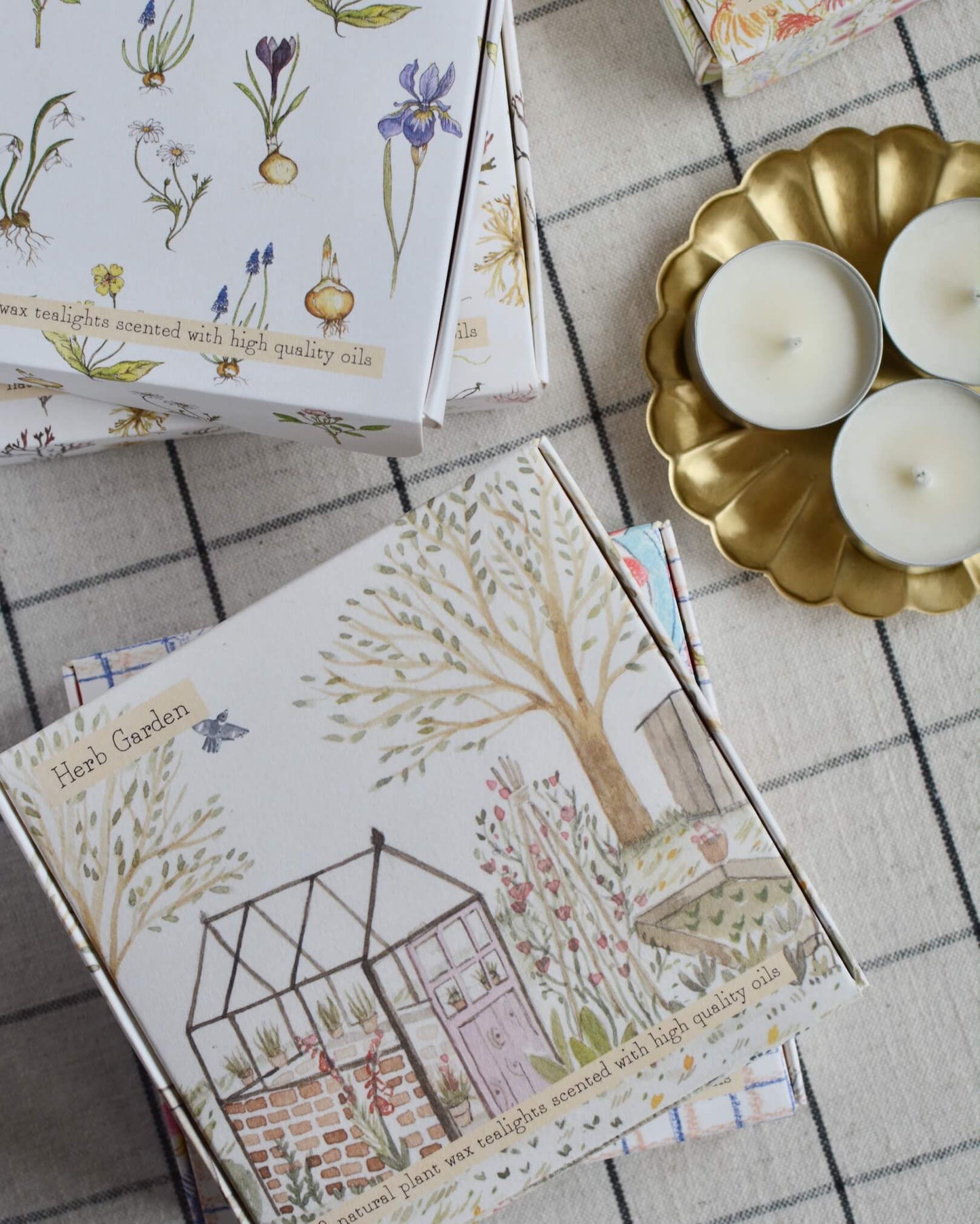 A collection of illustrated tea light boxes and a brass flower-shaped candle dish.