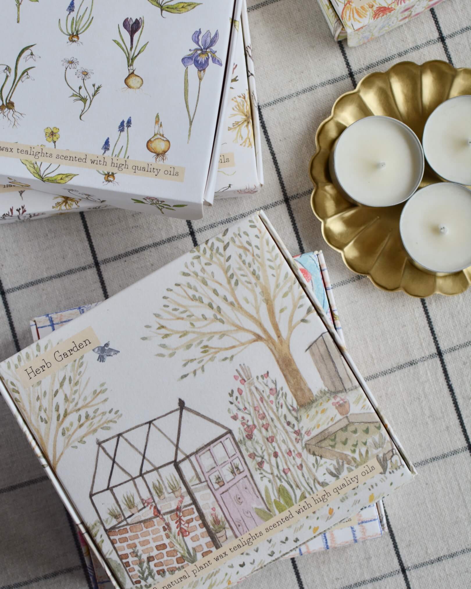 A collection of illustrated tea light boxes and a brass flower-shaped candle dish.