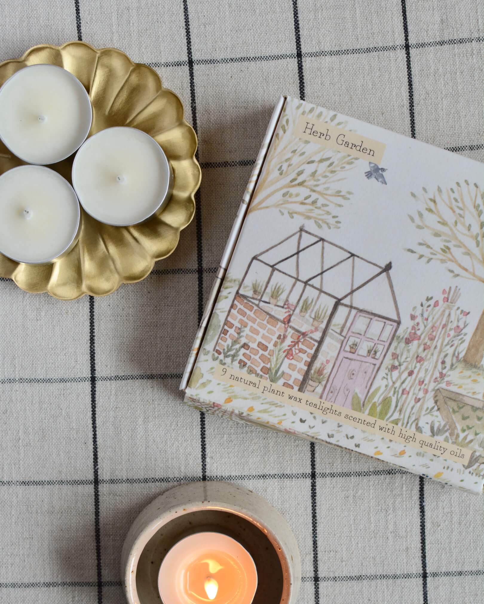 A box of tealights, with an illustrated box featuring a glasshouse within a summer garden.