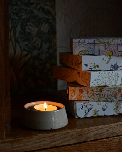 A lit scented tealight, inside of a ceramic tealight holder. 