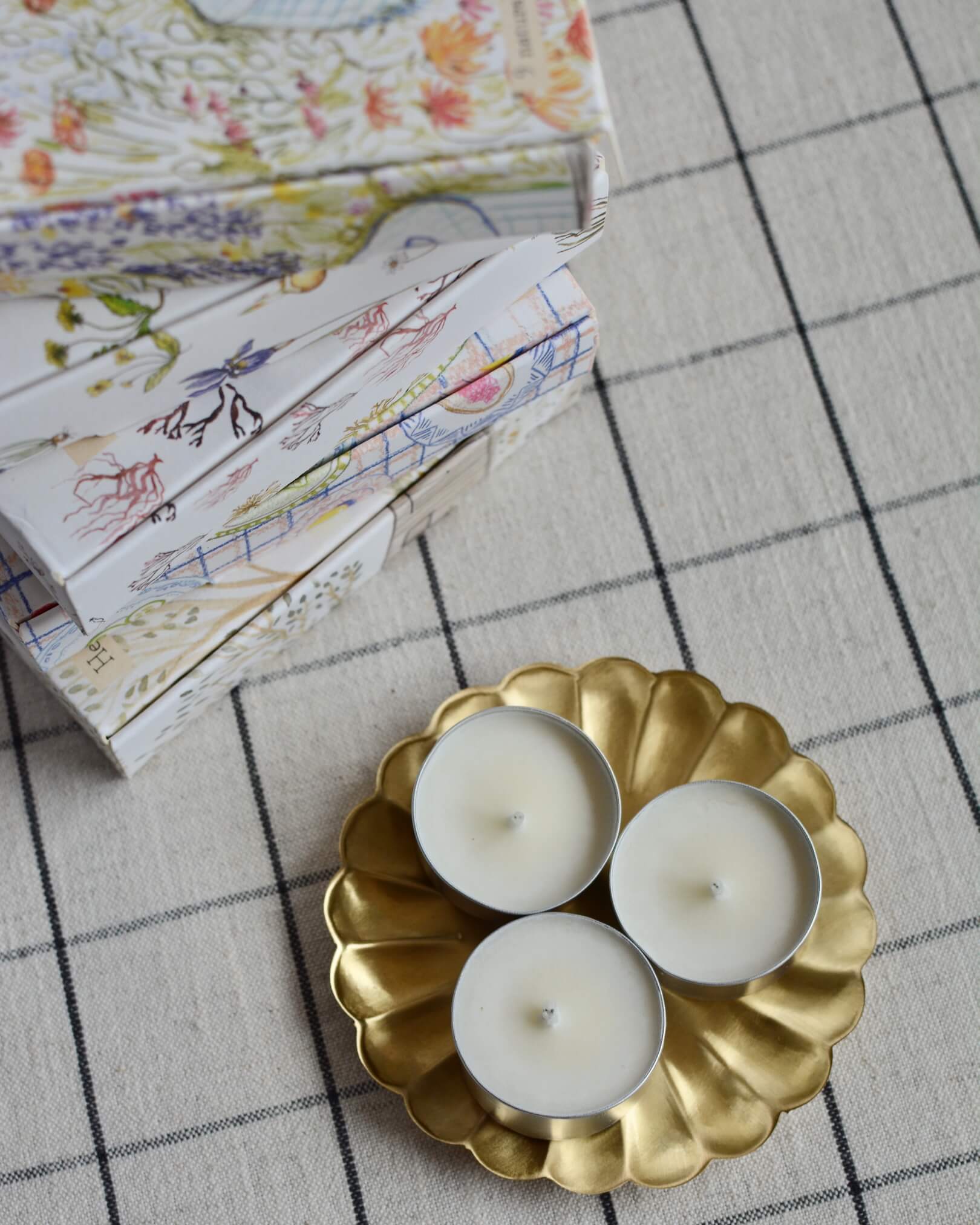 A collection of illustrated tea light boxes, alongside tea lights in a brass metal flower-shape dish.