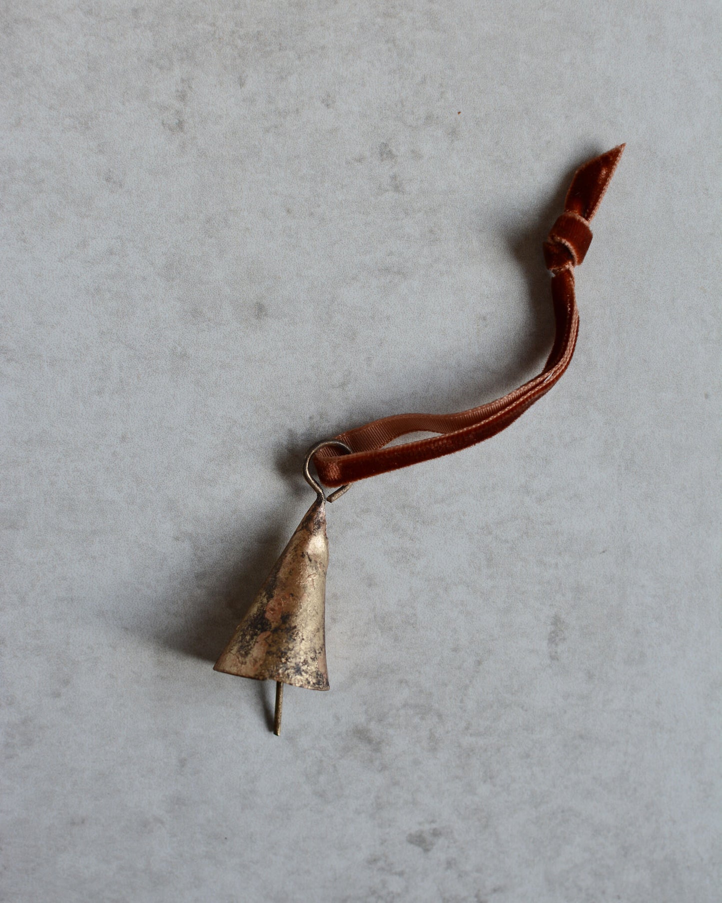 A brass bell ornament, strung onto a rust orange velvet ribbon.